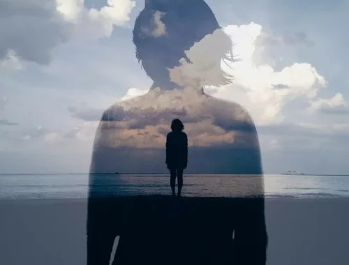 Silueta de una persona con un paisaje nublado reflejado, de pie junto al mar, simbolizando la introspección y la conexión con la naturaleza.