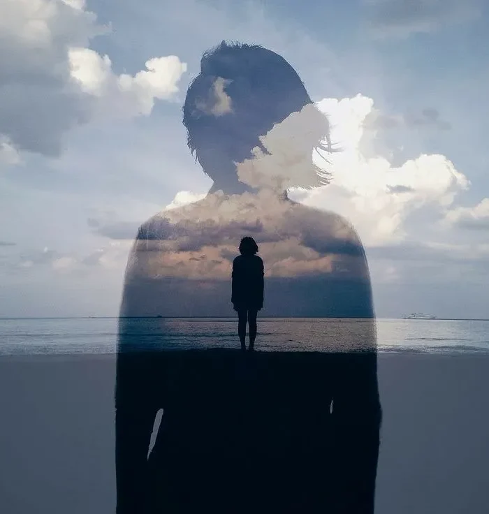 Silueta de una persona con un paisaje nublado reflejado, de pie junto al mar, simbolizando la introspección y la conexión con la naturaleza.