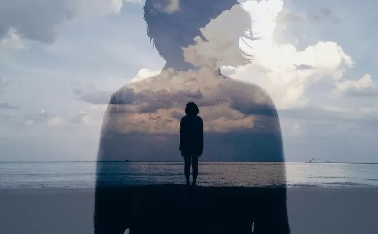 Silueta de una persona con un paisaje nublado reflejado, de pie junto al mar, simbolizando la introspección y la conexión con la naturaleza.